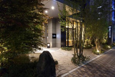 Der Eingangsbereich eines modernen Hotels in Osaka, umgeben von sanften Lichtern und üppigem Grün.