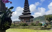 Ein balinesischer Tempel mit einer markanten, mehrstöckigen Dachstruktur, umgeben von blühenden Pflanzen und einem ruhigen Teich.