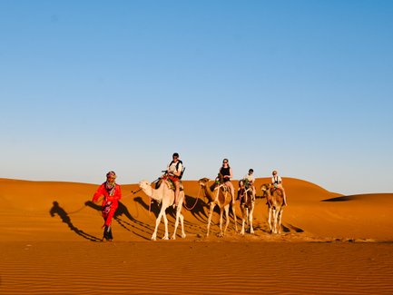 Familie zieht gemeinsam mit einer Kamelkarawane durch die Wüstenlandschaft der Sahara – Familienreise nach Marokko