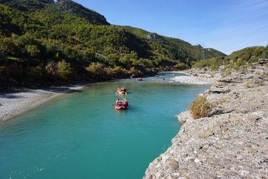 Eine Gruppe von Menschen paddelt in bunten Rafts auf einem klaren, türkisfarbenen Fluss, umgeben von grünen Hügeln.