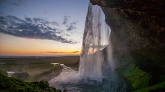Der majestätische Seljalandsfoss-Wasserfall stürzt in die Tiefe, umgeben von üppigem, grünem Gras und einem malerischen Sonnenuntergang.