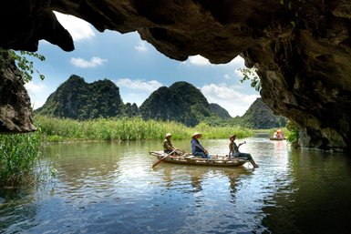 Drei Menschen sitzen in einem Boot auf einem ruhigen Gewässer, umgeben von üppiger Vegetation und beeindruckenden Felsen.