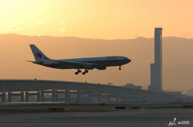 Ein Flugzeug landet majestätisch bei Sonnenuntergang über einer modernen Brücke und einer Stadtlandschaft im Hintergrund.