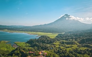 Ein majestätischer Vulkan erhebt sich über eine grüne Landschaft, umgeben von einem klaren blauen See und sanften Hügeln.