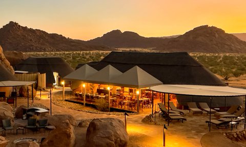 Eine malerische Aussicht auf das Twyfelfontein Adventure Camp, umgeben von majestätischen Bergen und sanften Hügeln.