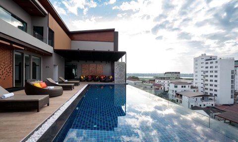 Ein luxuriöser Infinity-Pool spiegelt den Himmel wider, umgeben von modernen Liegen und bunten Sitzsäcken auf einer Dachterrasse.
