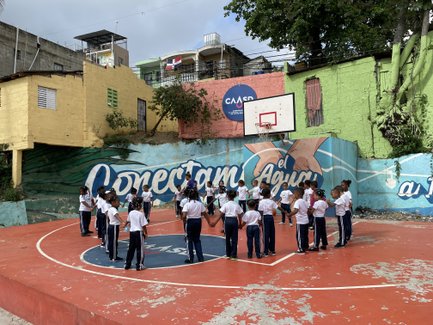 Eine Gruppe von Kindern in Sportkleidung versammelt sich auf einem Basketballplatz, um an einer Aktivität teilzunehmen.