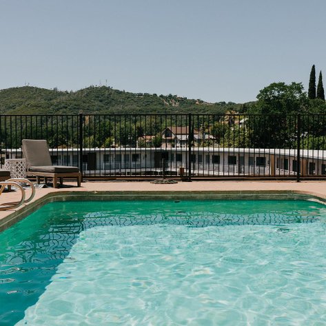 Ein klarer Pool mit grünem Wasser, umgeben von einem schwarzen Zaun und zwei Liegen, bietet einen Blick auf die Hügel.
