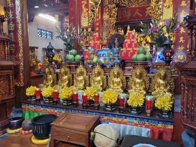 Eine prächtige Pagode mit goldenen Buddha-Statuen, umgeben von bunten Altären und frischen Früchten, strahlt spirituelle Ruhe aus.