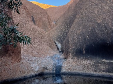 Ein ruhiger Wassersee spiegelt die beeindruckenden roten Felsen von Ayers Rock unter einem klaren blauen Himmel wider.