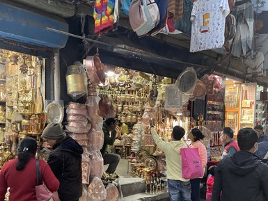 In einer belebten Straße in Kathmandu betrachten Menschen eine Vielzahl von Kupferwaren und Souvenirs in einem Geschäft.