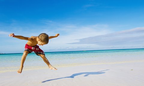 Junge springt am Sandstrand mit Blick auf das türkisfarbene Meer – Mexiko Reise mit Kindern