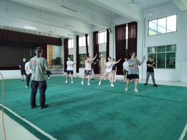 Eine Gruppe von Menschen übt Kung Fu in einem großen Raum mit grünem Teppich und großen Fenstern.