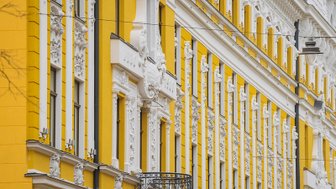 Die Fassade eines prächtigen gelben Gebäudes mit kunstvollen weißen Verzierungen und einem eleganten Balkon.
