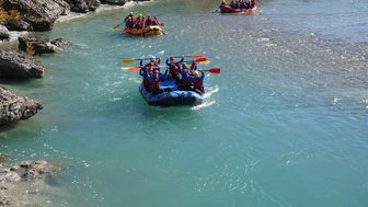 Eine Gruppe von Menschen paddelt fröhlich in einem blauen Raft auf einem klaren, türkisfarbenen Fluss.