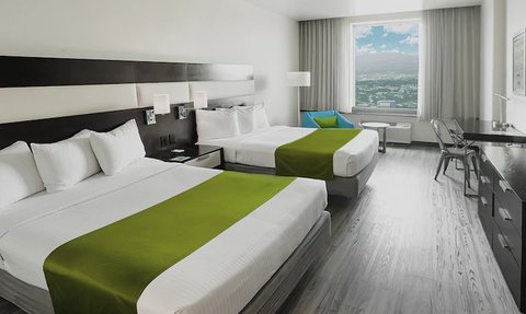 Ein modernes Hotelzimmer mit zwei Betten, grünem Bettzeug und einem großen Fenster, das einen Blick auf die Stadt bietet.