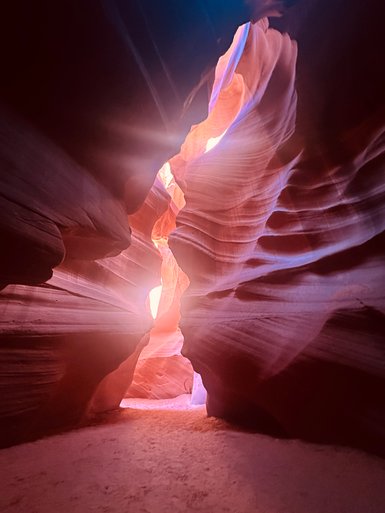 Ein schmaler Canyon mit sanften, rot-orangefarbenen Felswänden, die von Sonnenlicht durchflutet werden.