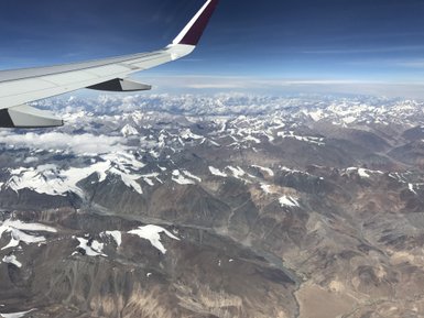 Ein Flugzeugflügel schneidet durch die Wolken über den majestätischen Himalaya-Gebirgen mit schneebedeckten Gipfeln.