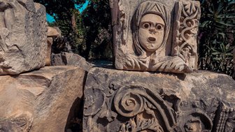 Ein kunstvoller Steinblock mit einer menschlichen Gesichtsreliefdarstellung und floralen Mustern im Hintergrund.