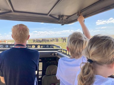 Eine Familie beobachtet Elefanten in der Ferne während einer Safari im Amboseli-Nationalpark, voller Staunen und Freude.