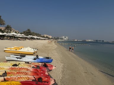 Am Strand stehen farbenfrohe Kajaks, während zwei Personen im Wasser spazieren gehen und die Sonne genießen.