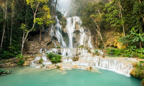 Majestätische Wasserfälle stürzen über Felsen, umgeben von üppigem Grün und sanftem, türkisfarbenem Wasser.