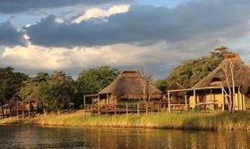 Eine friedliche Landschaft mit traditionellen Hütten am Ufer eines ruhigen Gewässers, umgeben von üppigem Grün.