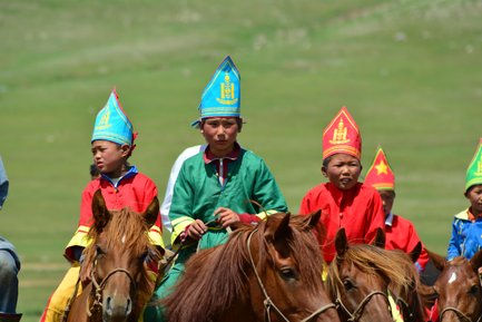 Eine Gruppe von Kindern in traditionellen bunten Gewändern reitet auf Pferden über eine grüne Wiese, voller Freude und Energie.