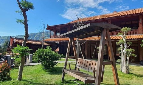 Ein schöner Garten mit einem Holzschaukelstuhl, umgeben von gepflegtem Gras und kleinen Bäumen unter einem blauen Himmel.