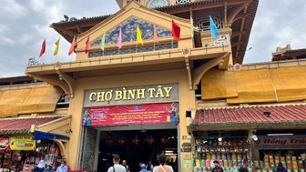 Der Eingang zum Chợ Bình Tây ist mit bunten Fahnen geschmückt, während Menschen geschäftig um die Stände herumgehen.