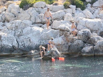 Eine Familie genießt einen sonnigen Tag am Meer, während Kinder auf den Felsen spielen und im Wasser planschen.