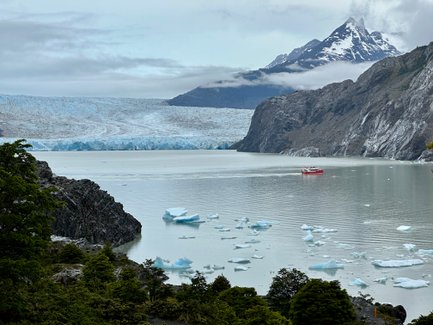 Ein rotes Boot fährt durch ruhiges Wasser, umgeben von schimmernden Eisbergen und majestätischen Bergen im Hintergrund.