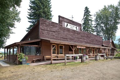 Ein rustikales Holzgebäude mit einem Schild, das den Namen 'Black Horse Saloon' zeigt, umgeben von Bäumen und Wiese.