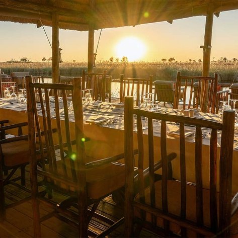 Ein eleganter Essbereich im Freien mit Holzstühlen, gedeckt für ein Abendessen bei Sonnenuntergang in Botswana.