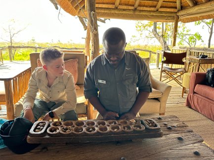 Ein Junge und ein Erwachsener spielen ein traditionelles Spiel mit einem Holzbrett und Steinen in einer gemütlichen Lodge.