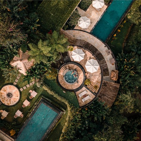 Ein luxuriöser Poolbereich in einem tropischen Garten, umgeben von üppigem Grün und Sonnenliegen unter Sonnenschirmen.