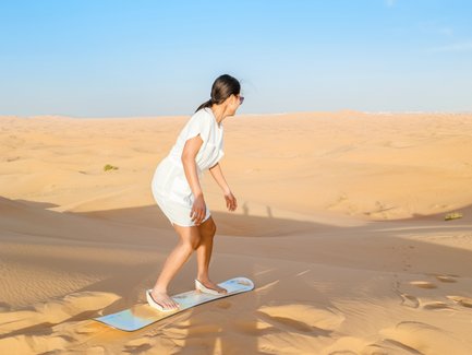 Teenager fährt Sandboard die Düne hinunter in der Wüste – Oman Reise mit Kindern
