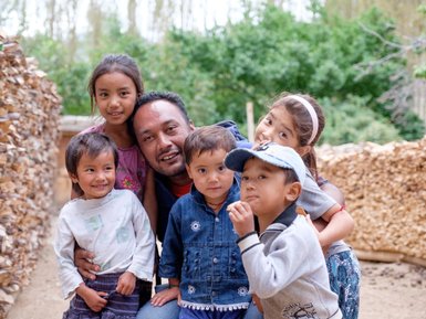 Eine fröhliche Familie posiert in einer ländlichen Umgebung, umgeben von Holzstapeln und grünen Bäumen im Hintergrund.
