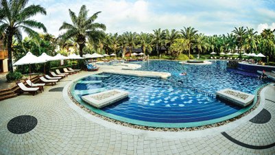 Ein weitläufiger Pool umgeben von Palmen und Liegen, ideal für Entspannung und Erholung in einem tropischen Resort.