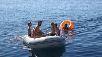 Eine Gruppe von Kindern und einem Erwachsenen fährt in einem Gummiboot auf dem ruhigen blauen Wasser des Meeres.