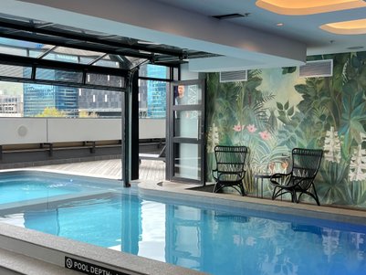 Ein eleganter Innenpool mit glattem Wasser, umgeben von einer tropischen Wandmalerei und modernen Möbeln.