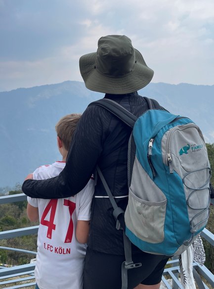 Eine Person mit einem Hut umarmt ein Kind, während sie auf eine beeindruckende Berglandschaft blicken.
