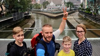 Familie posiert fröhlich für ein Selfie an der Flussmündung mit der Masjid Jamek im Hintergrund – Malaysia & Borneo Reise mit Kindern