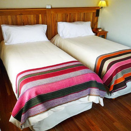 Zwei Einzelbetten mit bunten Decken stehen in einem hellen, gemütlichen Zimmer mit Holzdetails und sanfter Beleuchtung.