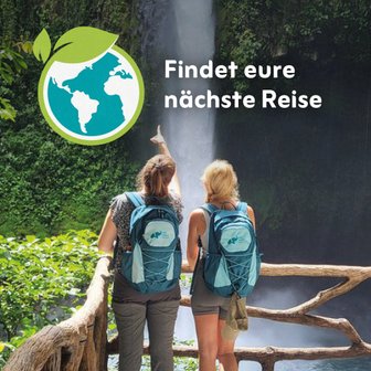 Zwei Frauen mit Rucksäcken stehen an einem Wasserfall und zeigen auf die beeindruckende Natur um sie herum.