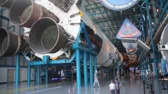 Im Kennedy Space Center stehen zwei Kinder fasziniert vor einem riesigen Raketenmotor, während Besucher im Hintergrund umhergehen.