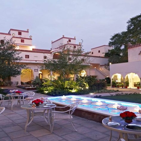 Ein eleganter Innenhof mit einem beleuchteten Pool, umgeben von üppigem Grün und traditioneller Architektur in Jaipur.