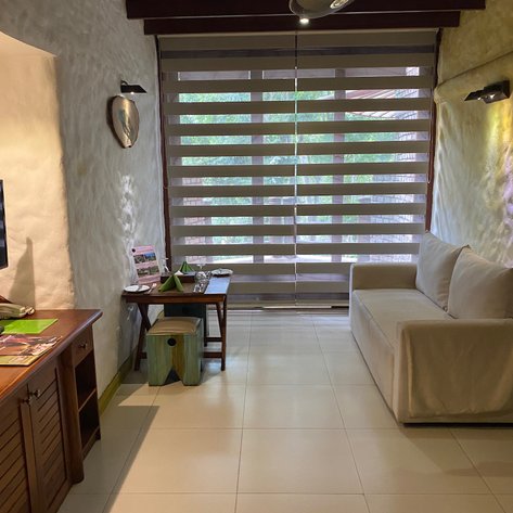 Ein gemütlicher Raum mit einem weißen Sofa, einem Holztisch und einem kleinen Hocker, beleuchtet von sanftem Licht.