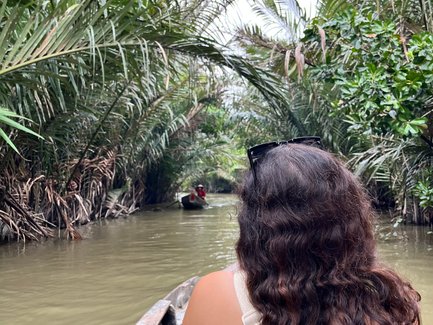 Eine Person mit lockigem Haar sitzt in einem Boot und genießt die ruhige Fahrt durch einen grünen Wasserweg im Mekong-Delta.