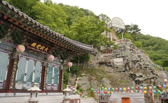 Ein traditionelles Gebäude mit bunten Laternen steht vor einer bewaldeten Felslandschaft, die mit festlichen Dekorationen geschmückt ist.